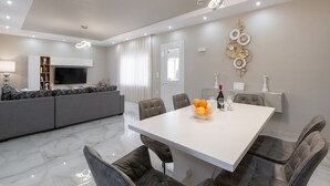 A modern dining area with a white table, leather chairs, and a bowl of fruit. - The  Cottage South  Escape  with beach front pool (Plimmiri)