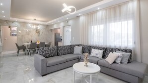 A modern living room with a grey sectional sofa, a round coffee table, and a dining area with a white table and chairs. - The  Cottage South  Escape  with beach front pool (Plimmiri)