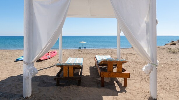 A beach setting with a white canopy structure, two wooden lounge chairs, and a red kayak on the sand. - The  Cottage South  Escape  with beach front pool (Plimmiri)