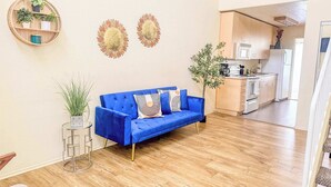 A modern living room with a blue sofa, a round wall shelf with plants, and decorative wall art.