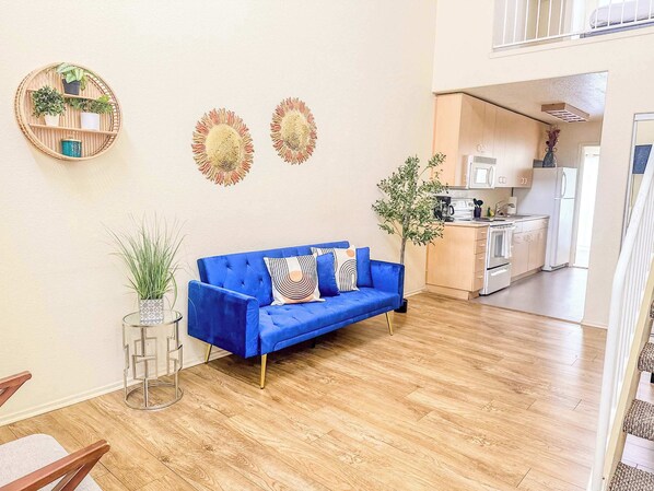 Una sala de estar moderna con un sofá azul, una estantería redonda con plantas y decoración en la pared.