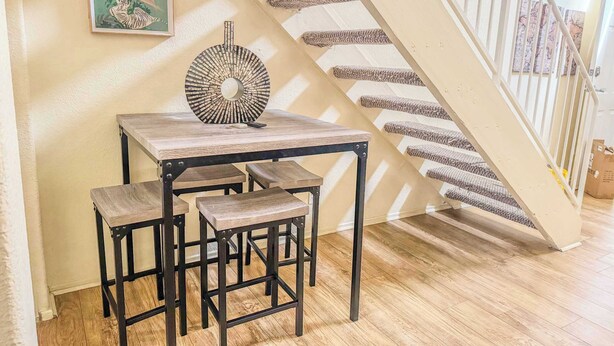 A dining area with a table and benches, a decorative wall piece, and a staircase with a striped carpet.