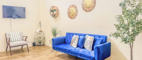 Una sala de estar con un sofá azul, un televisor, una planta y decoración en la pared.