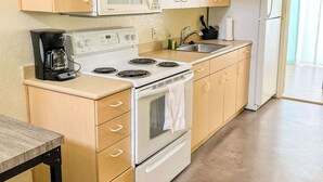A compact kitchen with wooden cabinets, a white stove, a microwave, a refrigerator, and a coffee maker.