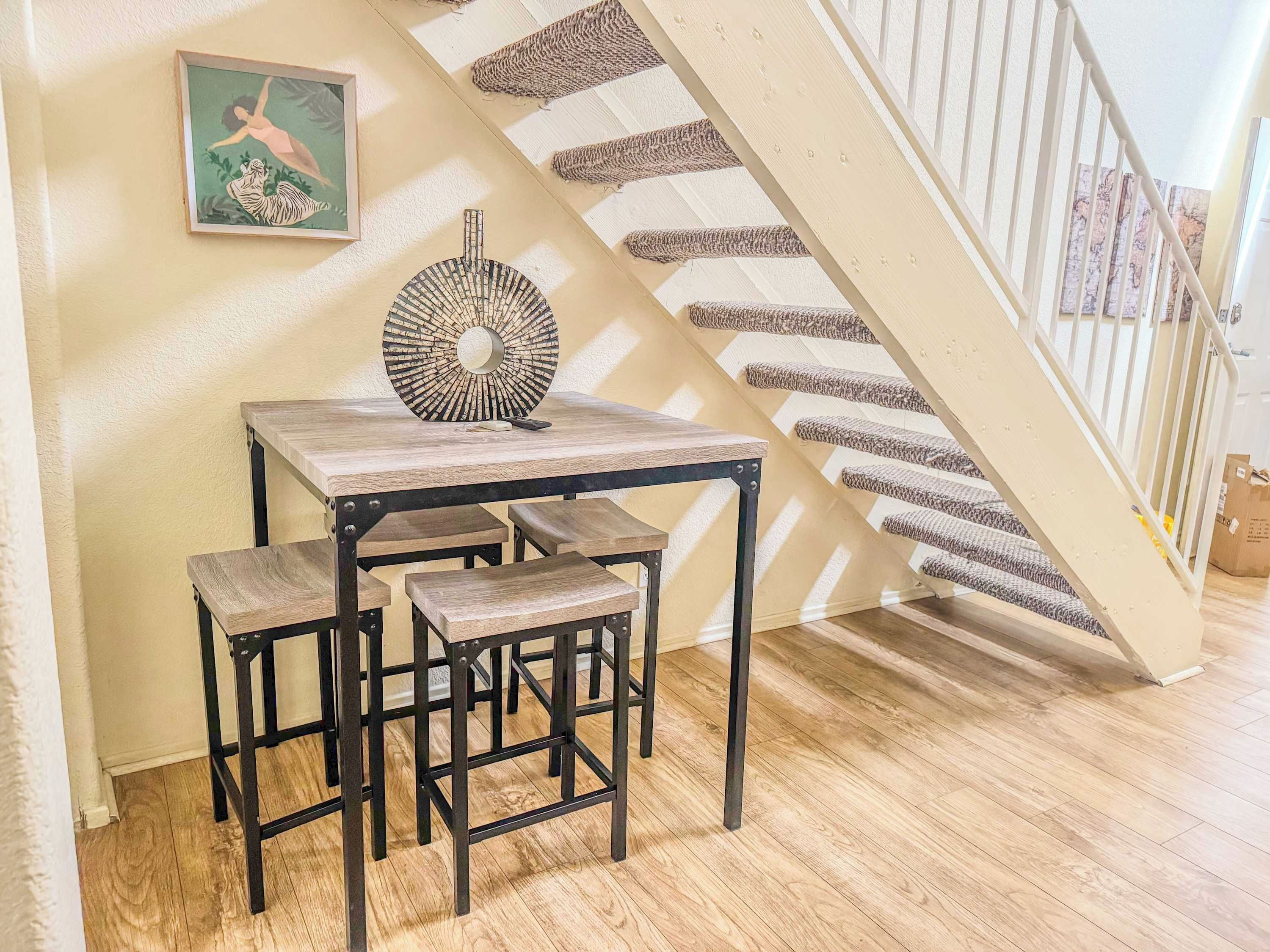 A dining area with a table and benches, a decorative wall piece, and a staircase with a striped carpet.