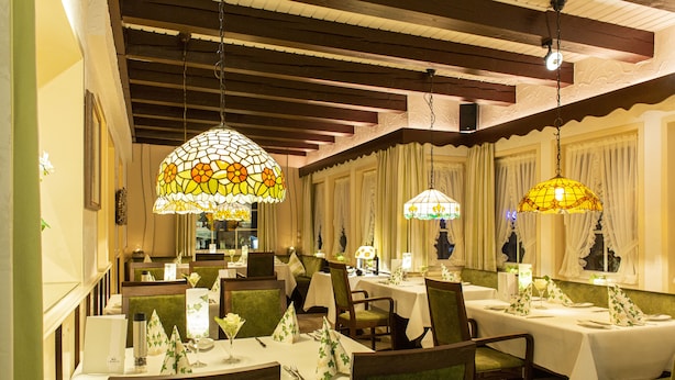 A restaurant with multiple tables, green upholstered chairs, and decorative stained glass lamps. - Lampes Posthotel (Delligsen)