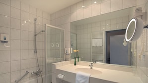 A modern bathroom with a glass shower enclosure, a large mirror, and a white sink. - Lampes Posthotel (Delligsen)