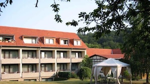 A multi-story hotel with a red roof, balconies, and a grassy courtyard with a tent. - Lampes Posthotel (Delligsen)