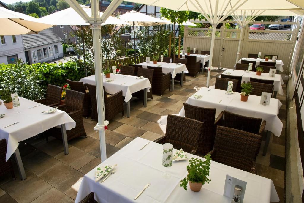 Eine Terrasse im Freien mit Tischen und Stühlen, beschattet durch Sonnenschirme, umgeben von Grünpflanzen.