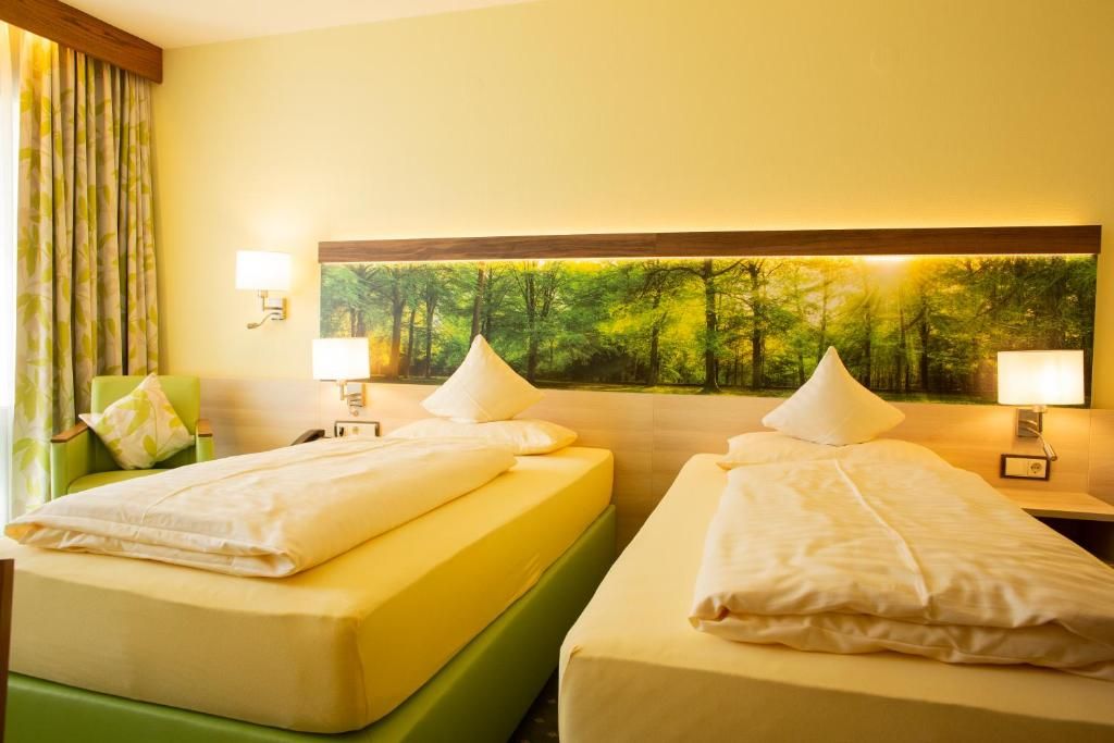 Ein Hotelzimmer mit zwei Betten, einem großen Wandbild mit Waldmotiv und zwei Nachttischlampen.
