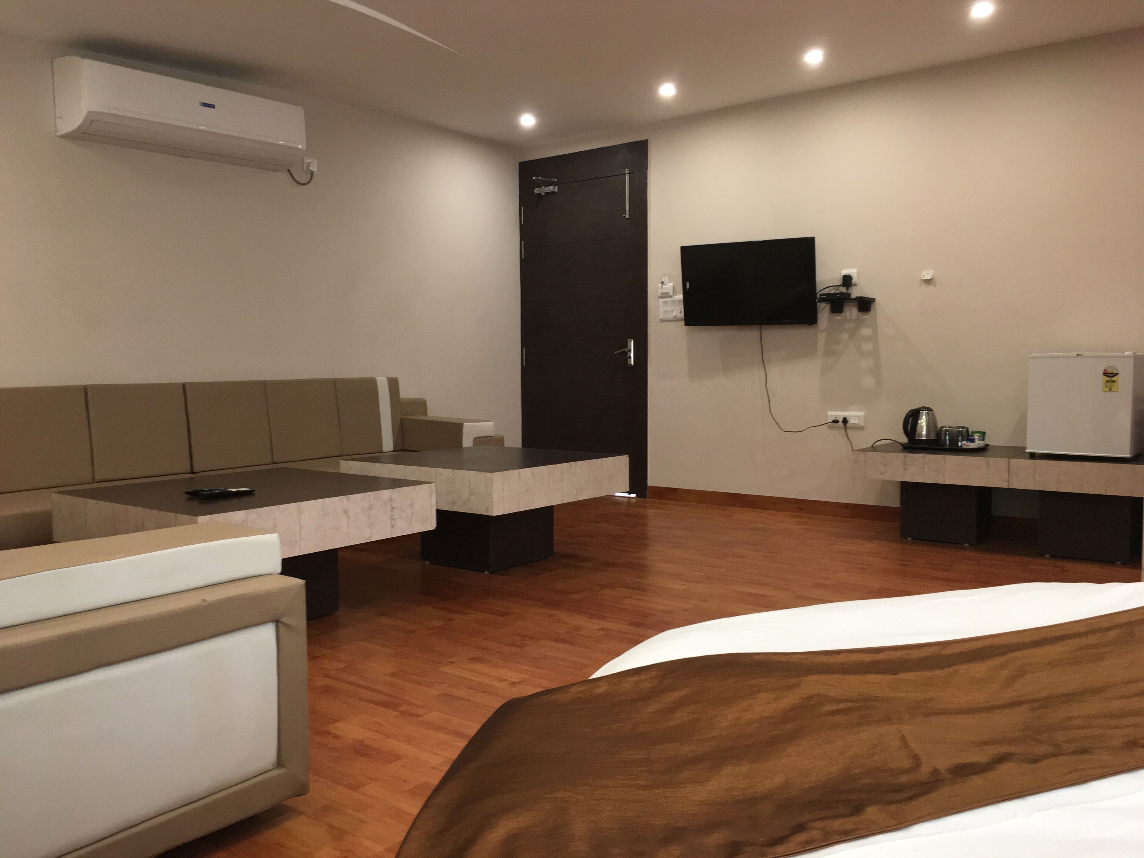 A hotel room with a bed, a sofa, a small table, a TV, and a refrigerator.