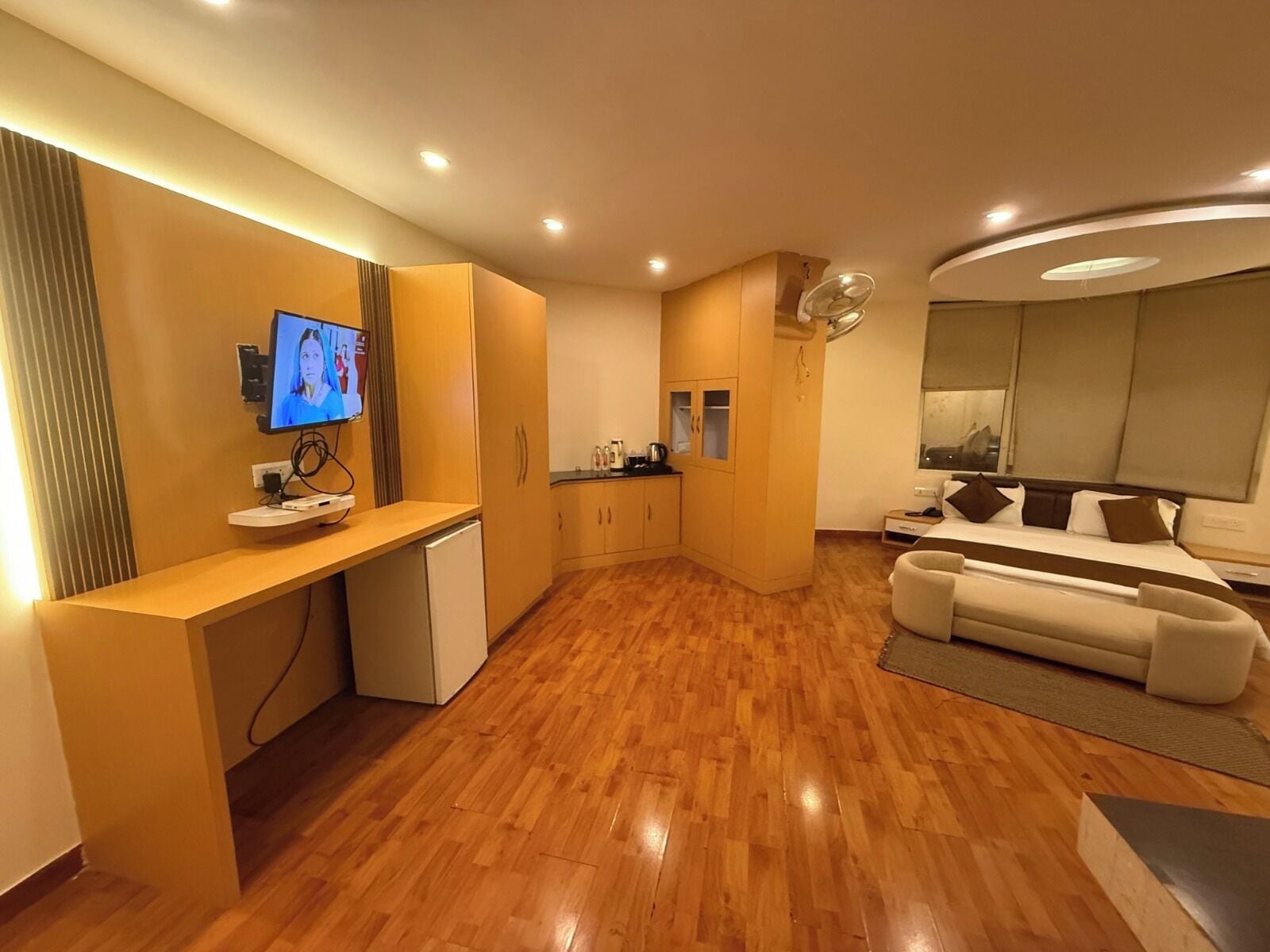 A modern living room with a wooden floor, a sofa, a TV, a kitchen area, and a dining table.