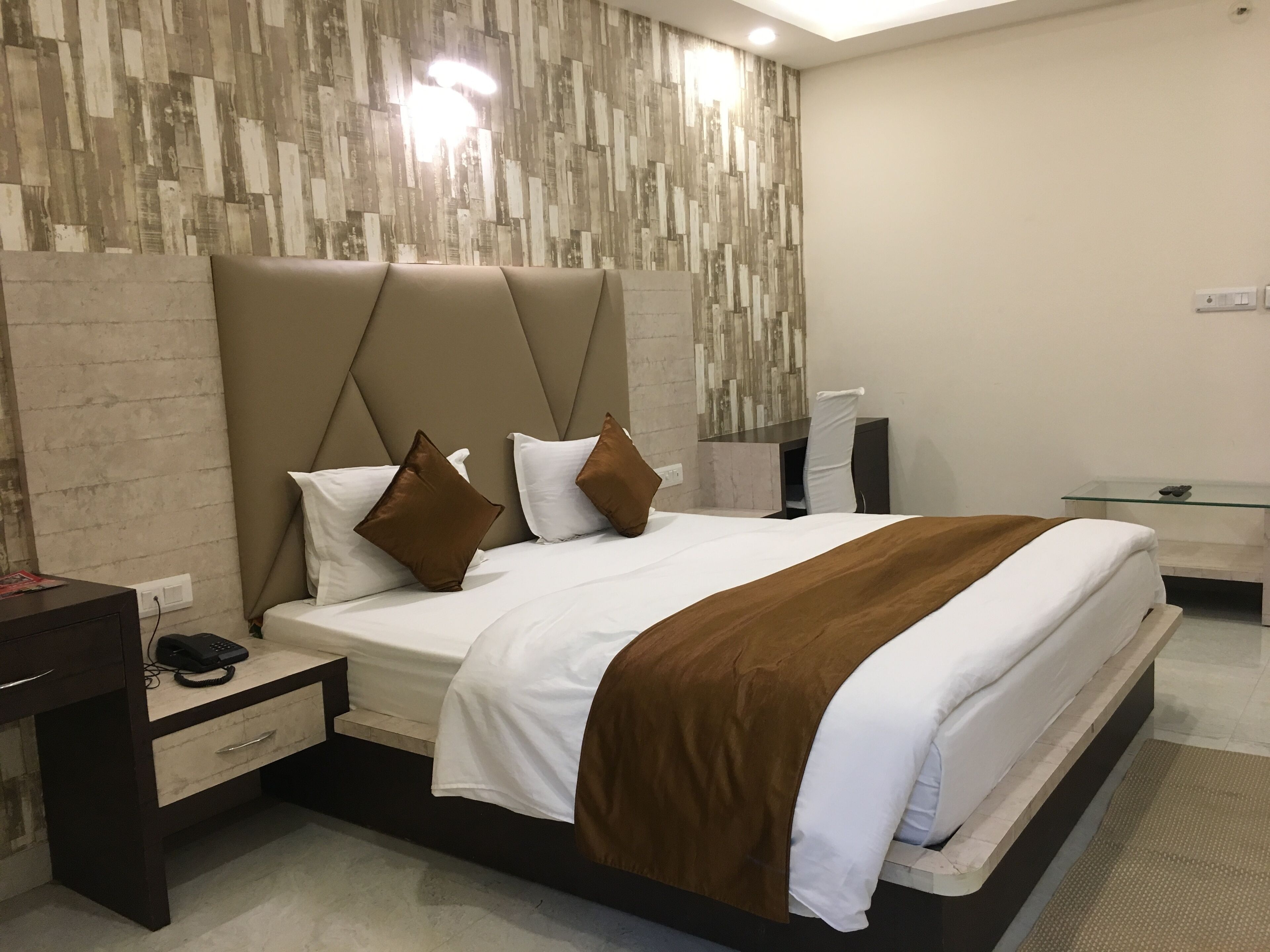 Una camera d'albergo moderna con un letto grande, un comodino con il telefono, una scrivania e una sedia.