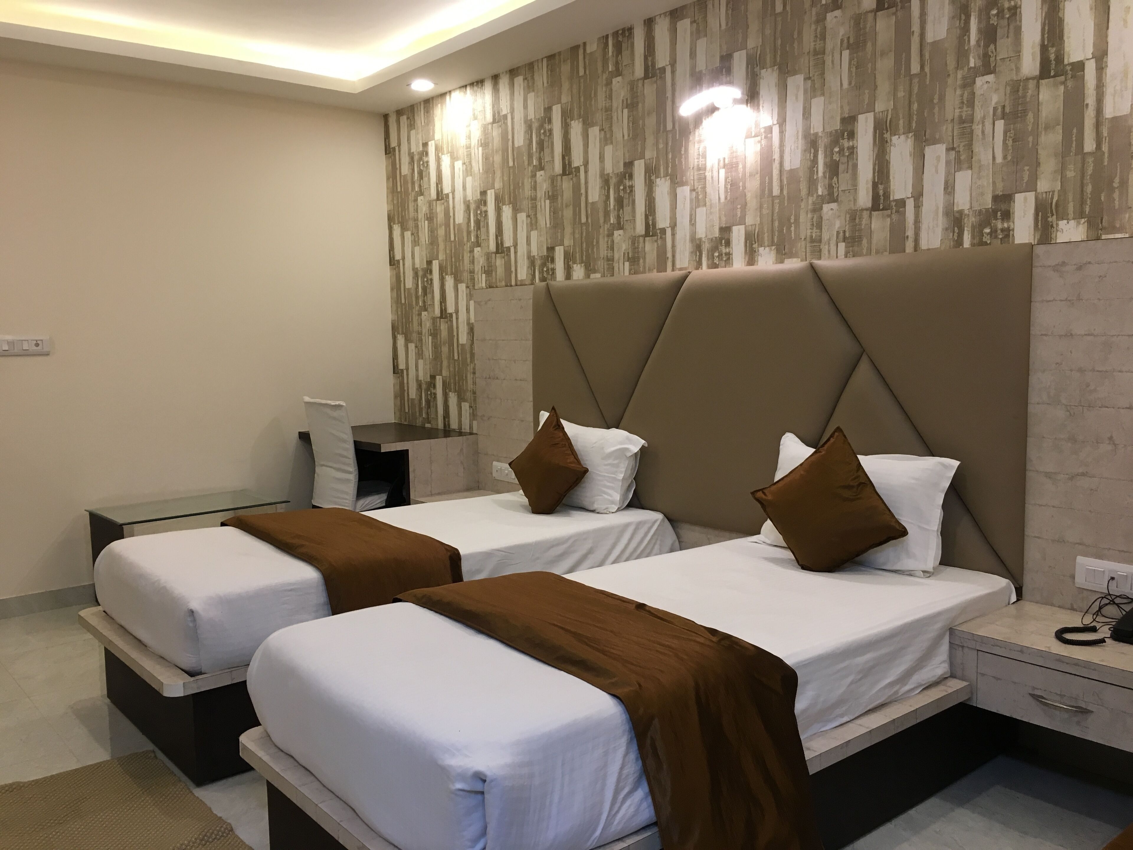Una habitación de hotel moderna con dos camas, un escritorio y una pared con diseño imitación madera.