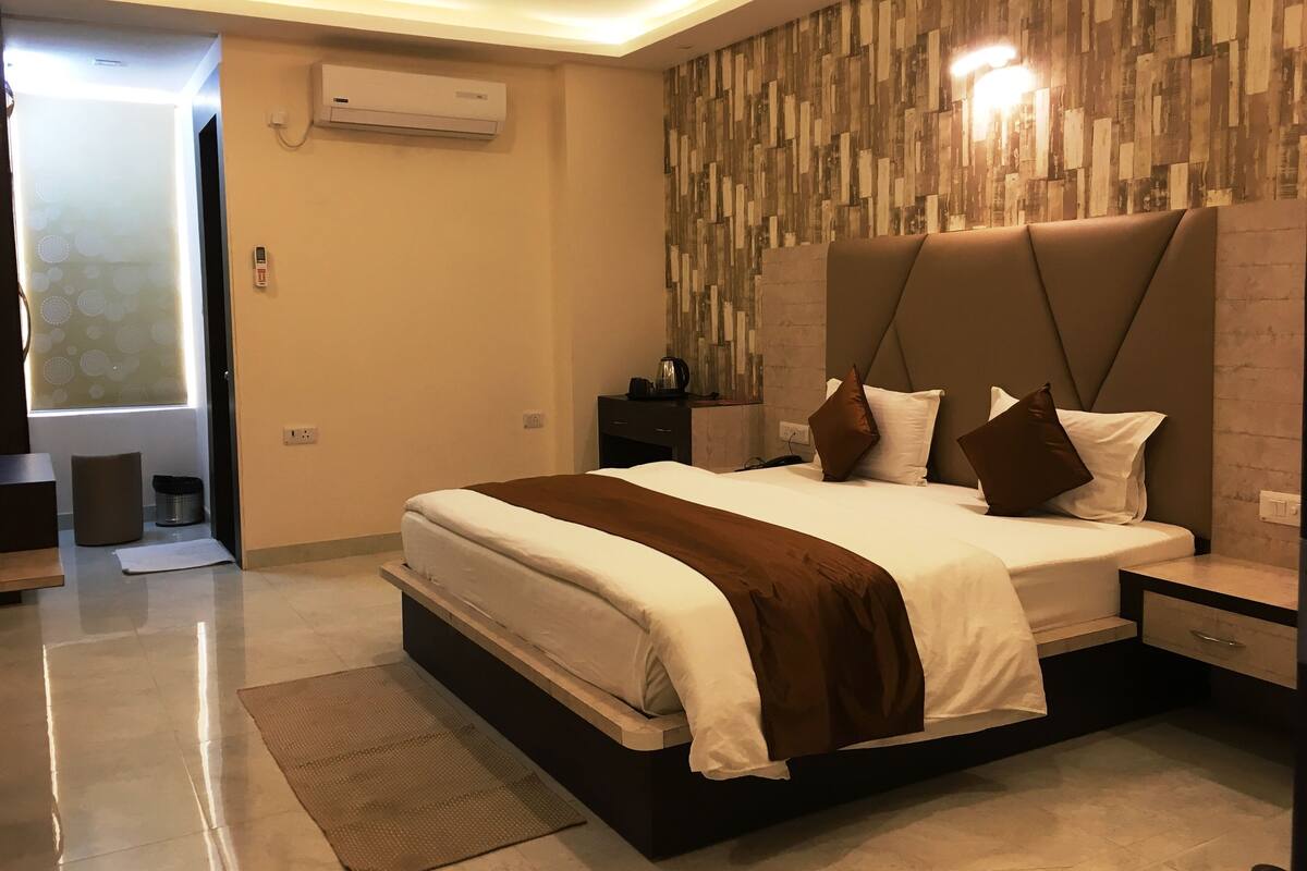 A modern bedroom with a large bed, a nightstand, a wall-mounted air conditioner, and a window with a view.