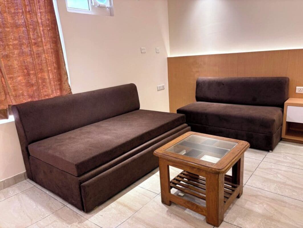 A living room with a brown sofa, a glass-top coffee table, and a wooden side table.