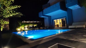 Un bâtiment moderne doté d’une piscine, illuminée par un éclairage artificiel, de nuit.