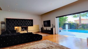Un salon moderne avec une cheminée, un grand canapé noir et une vue sur une piscine.