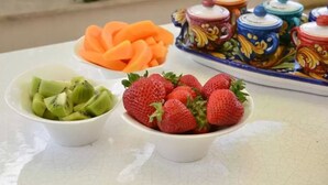 A table with bowls of sliced kiwi and strawberries, and a decorative ceramic set with lids. - B&B Talìa (Grammichele)