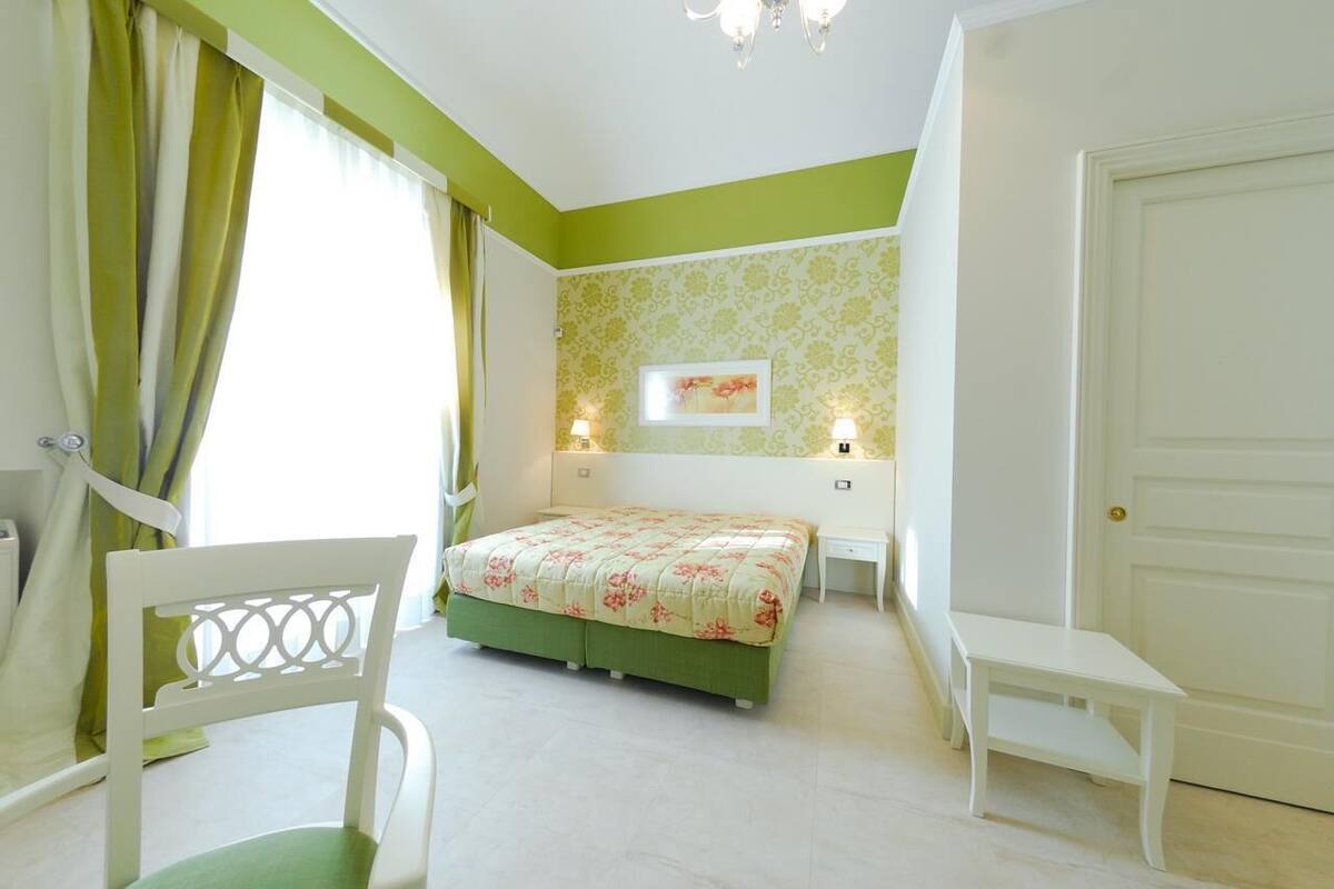 A bedroom with a bed, a chair, a bedside table, and a door.