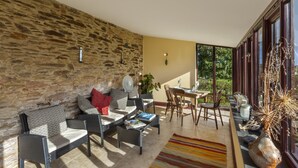 Un vaste espace de vie agrémenté d’un mur en pierre, de meubles en osier, d’une table à manger et offrant une vue dégagée grâce à de grandes fenêtres.