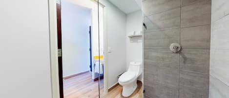 Uma casa de banho moderna com sanita, chuveiro e soalho em madeira.