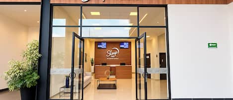 The entrance to a Sleep Inn hotel with a reception desk, a television, and a green exit sign.