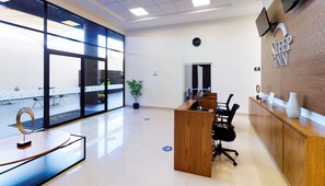 A modern hotel reception area with a wooden reception desk, black office chairs, a clock on the wall, and large windows offering a view of the outside. - Sleep Inn Queretaro (Querétaro)
