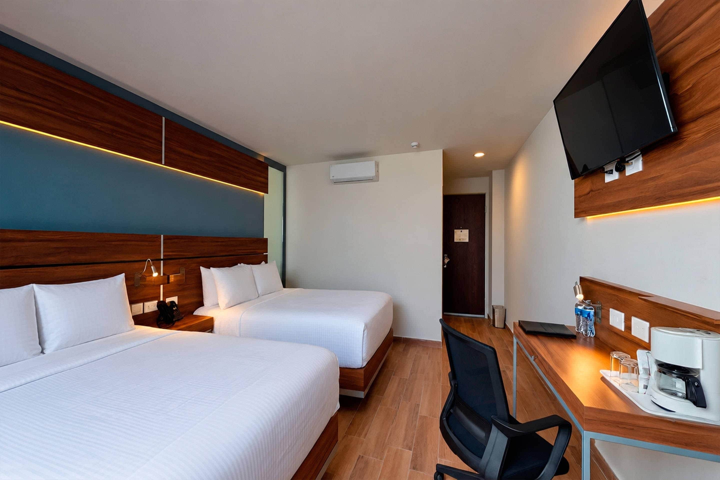 Habitación de hotel con dos camas, un escritorio con silla, un televisor y una cafetera.