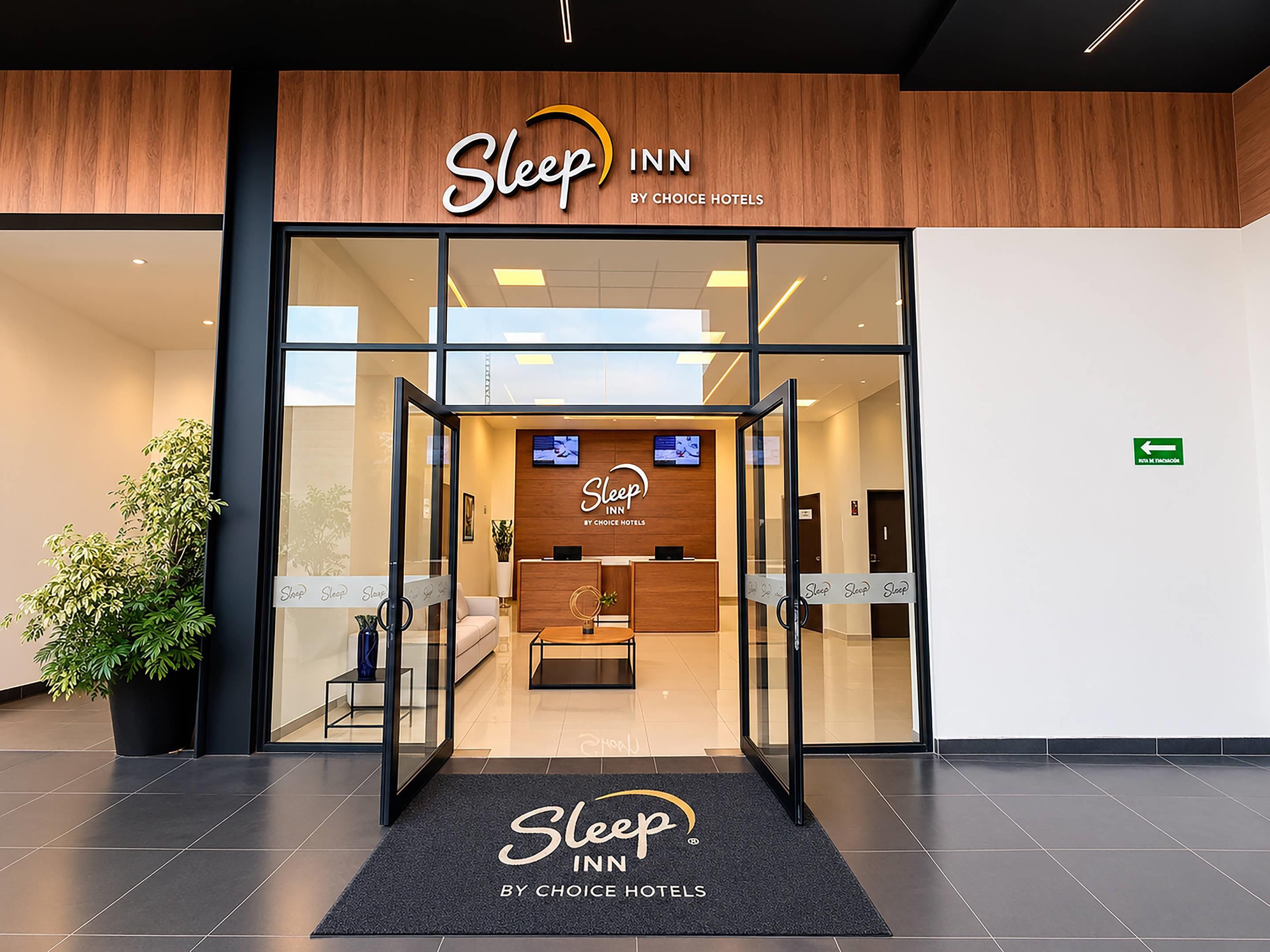 La entrada a un Sleep Inn de Choice Hotels, con una recepción, un televisor y una planta afuera.