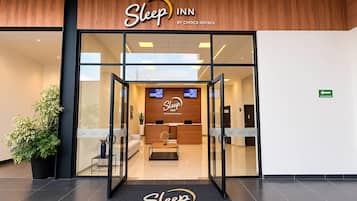 Entrada de um Sleep Inn da Choice Hotels, com uma receção, uma televisão e uma planta do lado de fora.