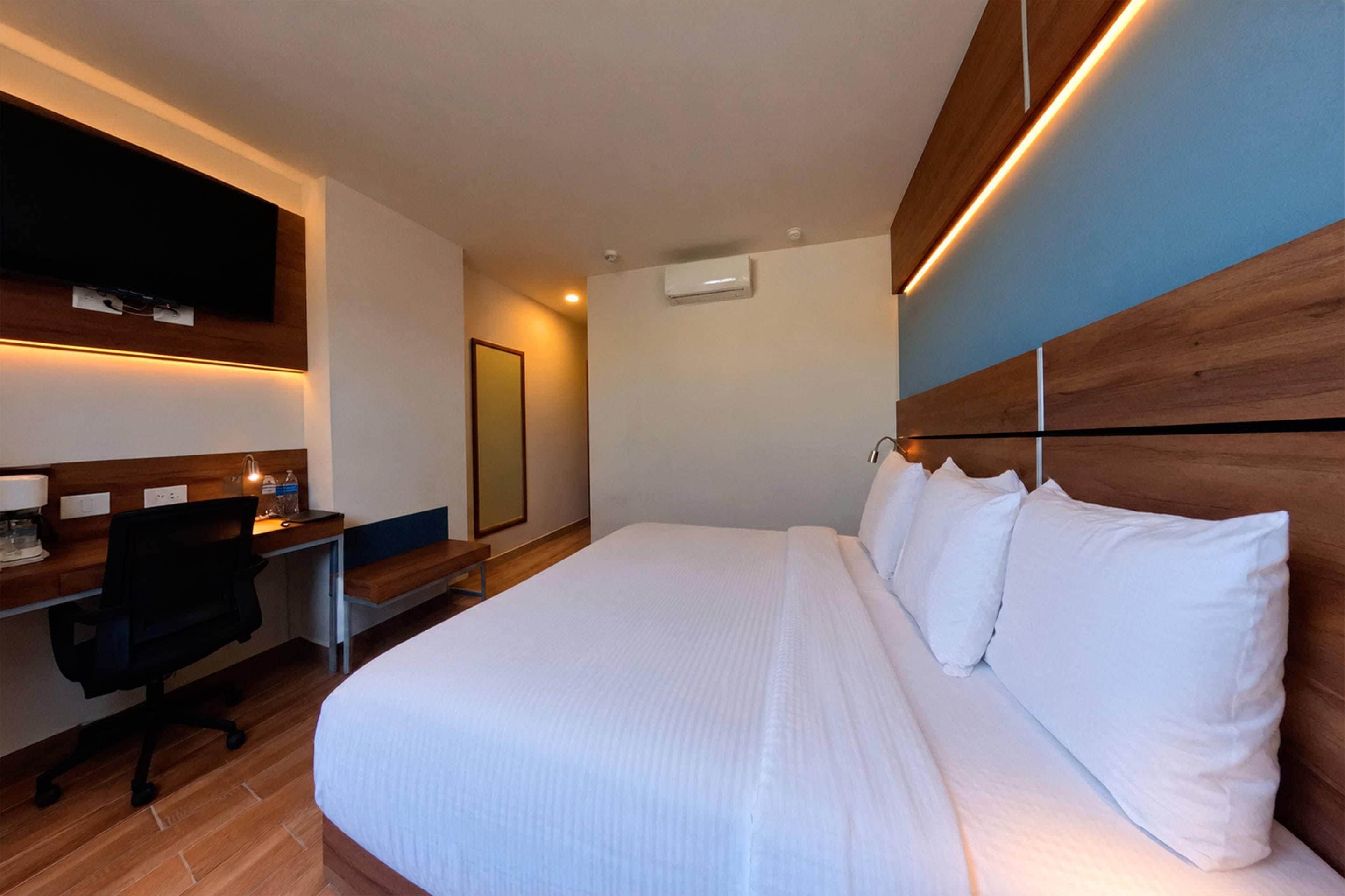 A hotel room with a bed, a desk, a chair, and a television mounted on the wall.