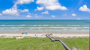 A beach with a wooden walkway leading to the water, a tent, and a blue umbrella.