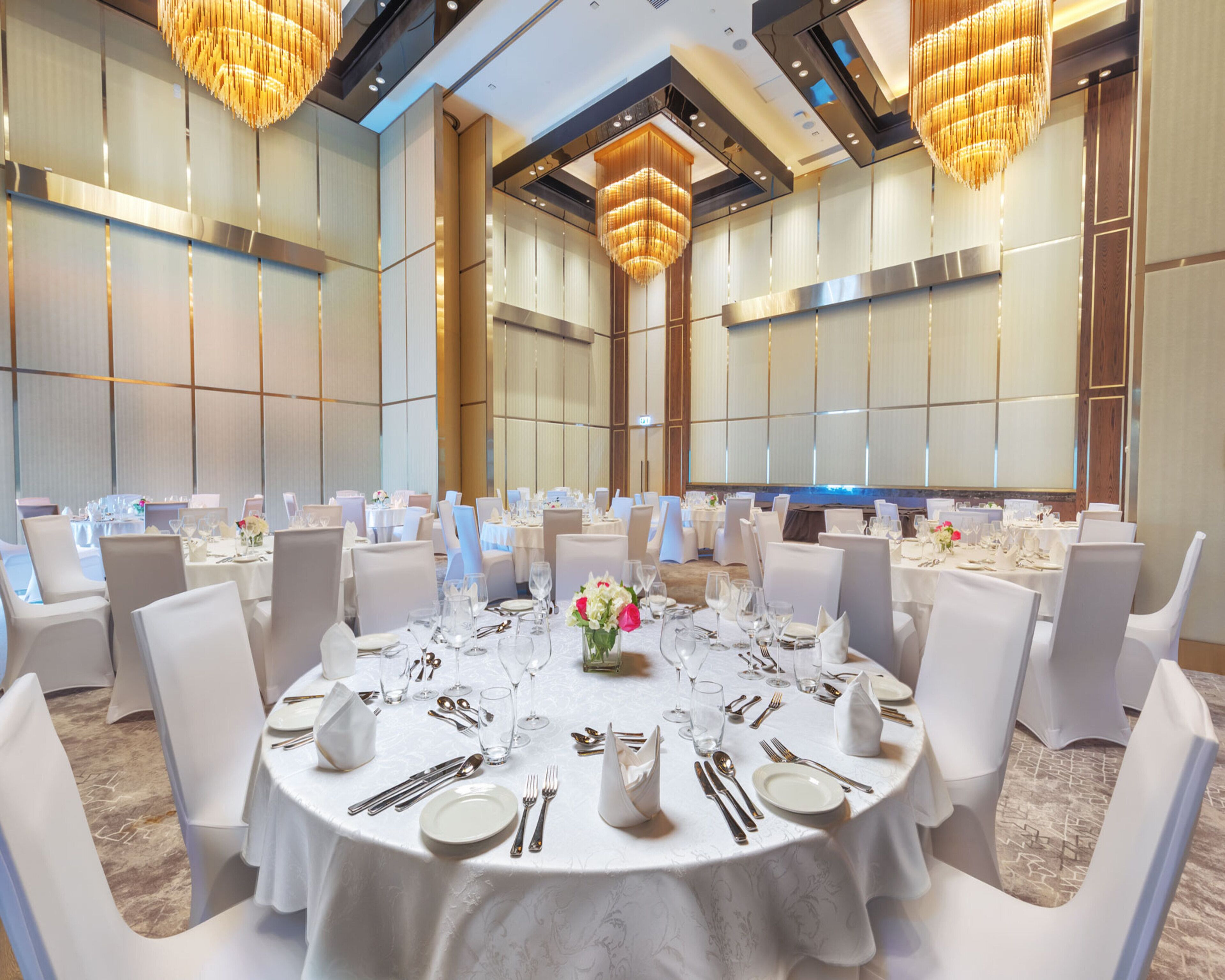 A banquet hall with round tables set for dining, white chairs, and chandeliers.