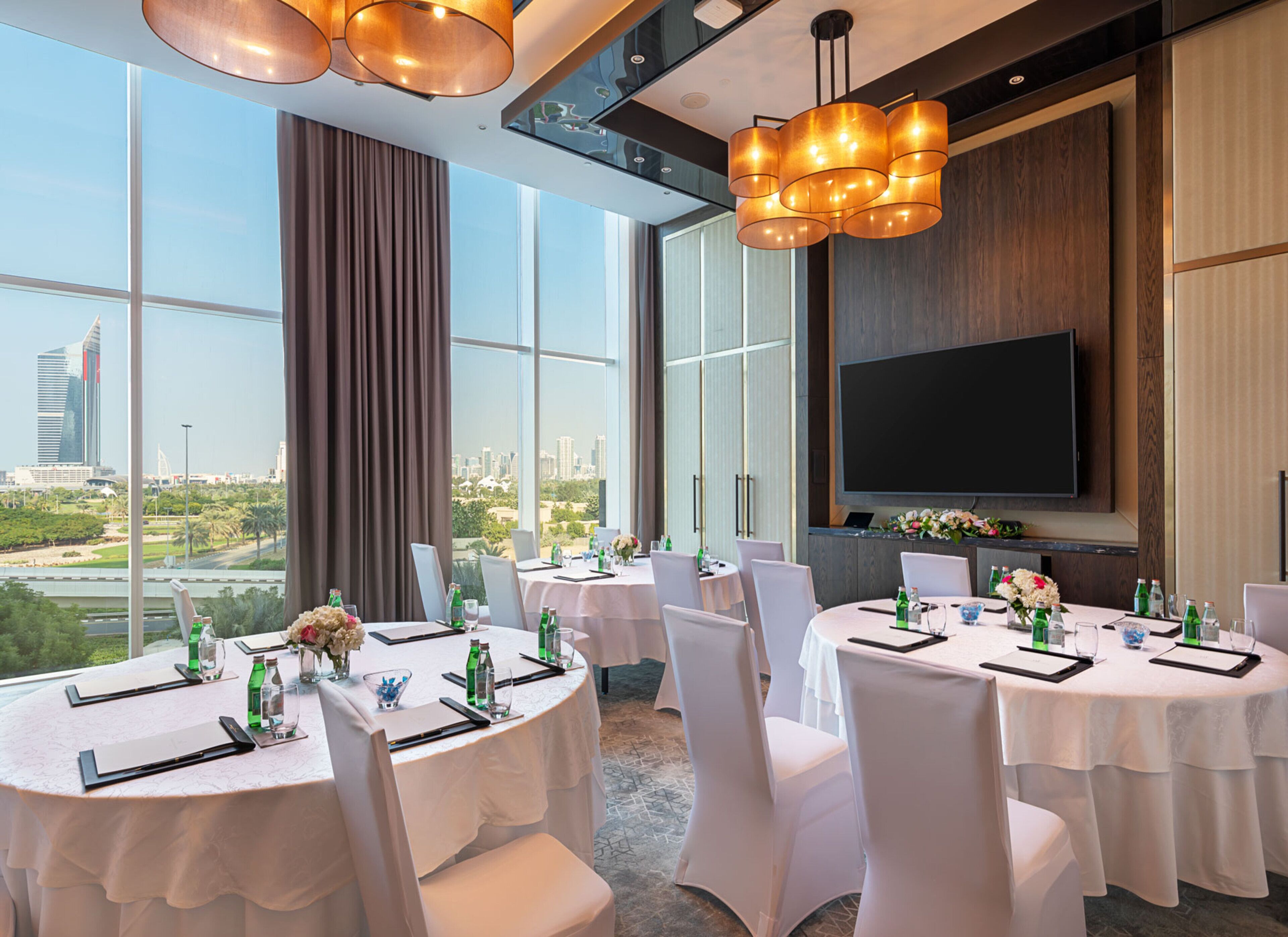 A conference room with round tables, white chairs, and a large TV screen.