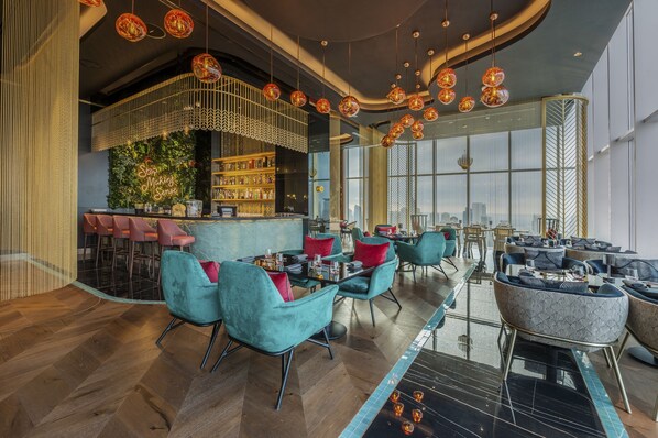Un área de bar moderna con asientos, una barra y vistas a la ciudad a través de amplios ventanales.