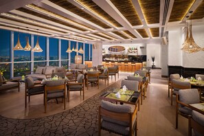 A modern lounge area with a bar, seating arrangements, and large windows offering a city view.