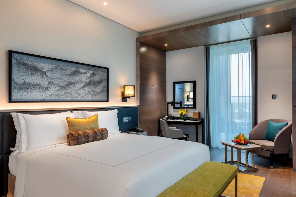 Habitació d'hotel moderna amb un llit gran, un escriptori, una cadira i vista a la ciutat a través de grans finestres.