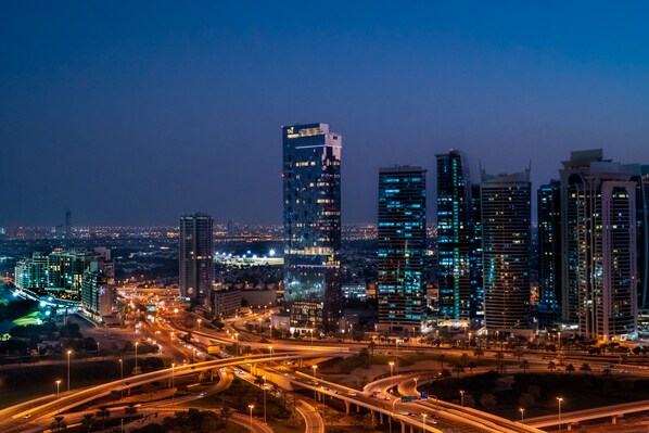 A cityscape at dusk with illuminated skyscrapers and a busy highway.