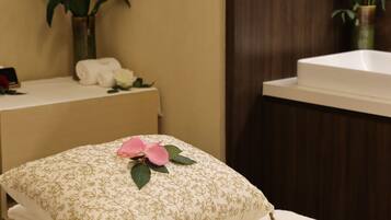 A neatly arranged room with a bed, a small table with towels and a vase of flowers, and a wooden panel wall.
