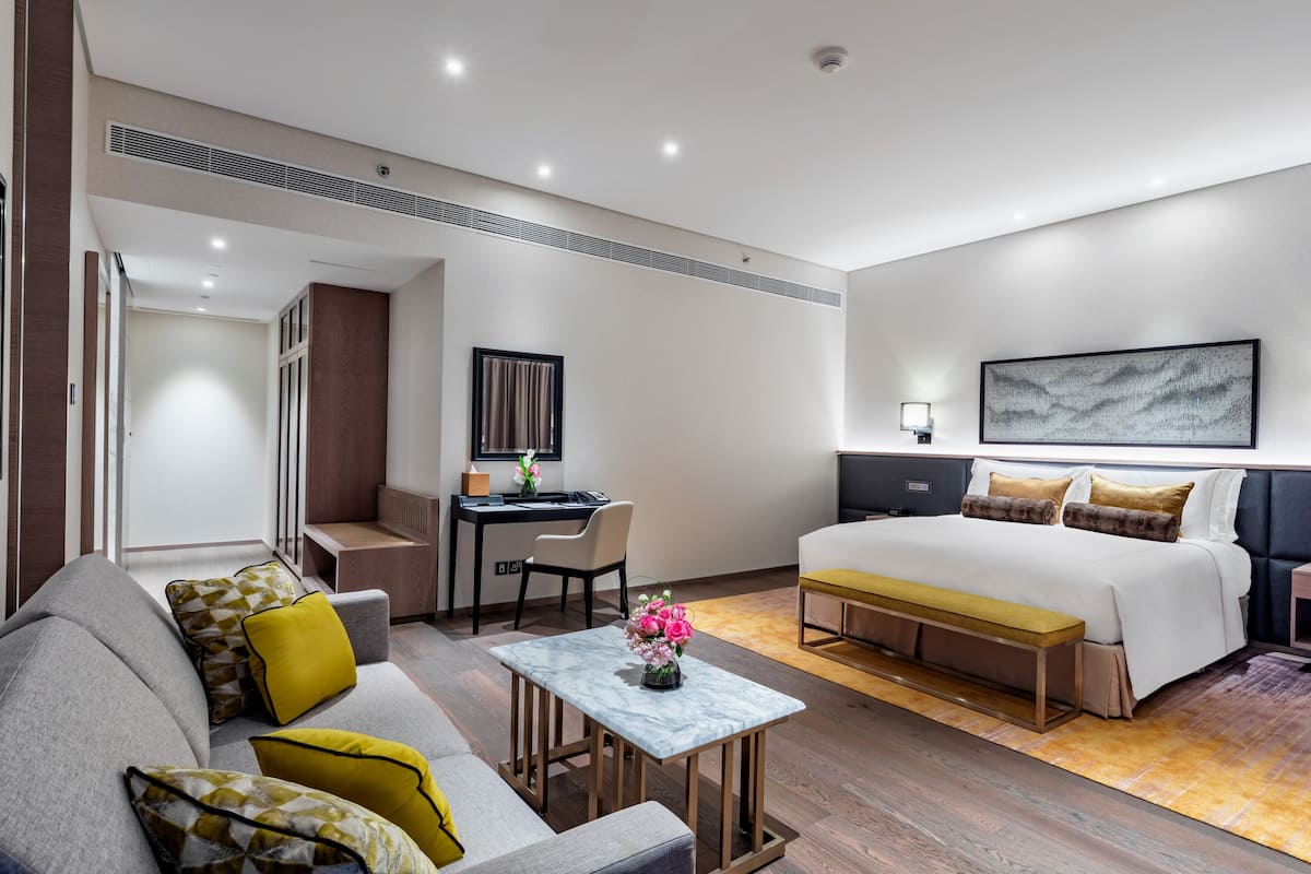 Habitació d'hotel moderna amb un llit, una escriptori, un sofà i una taula petita amb un ram de flors.