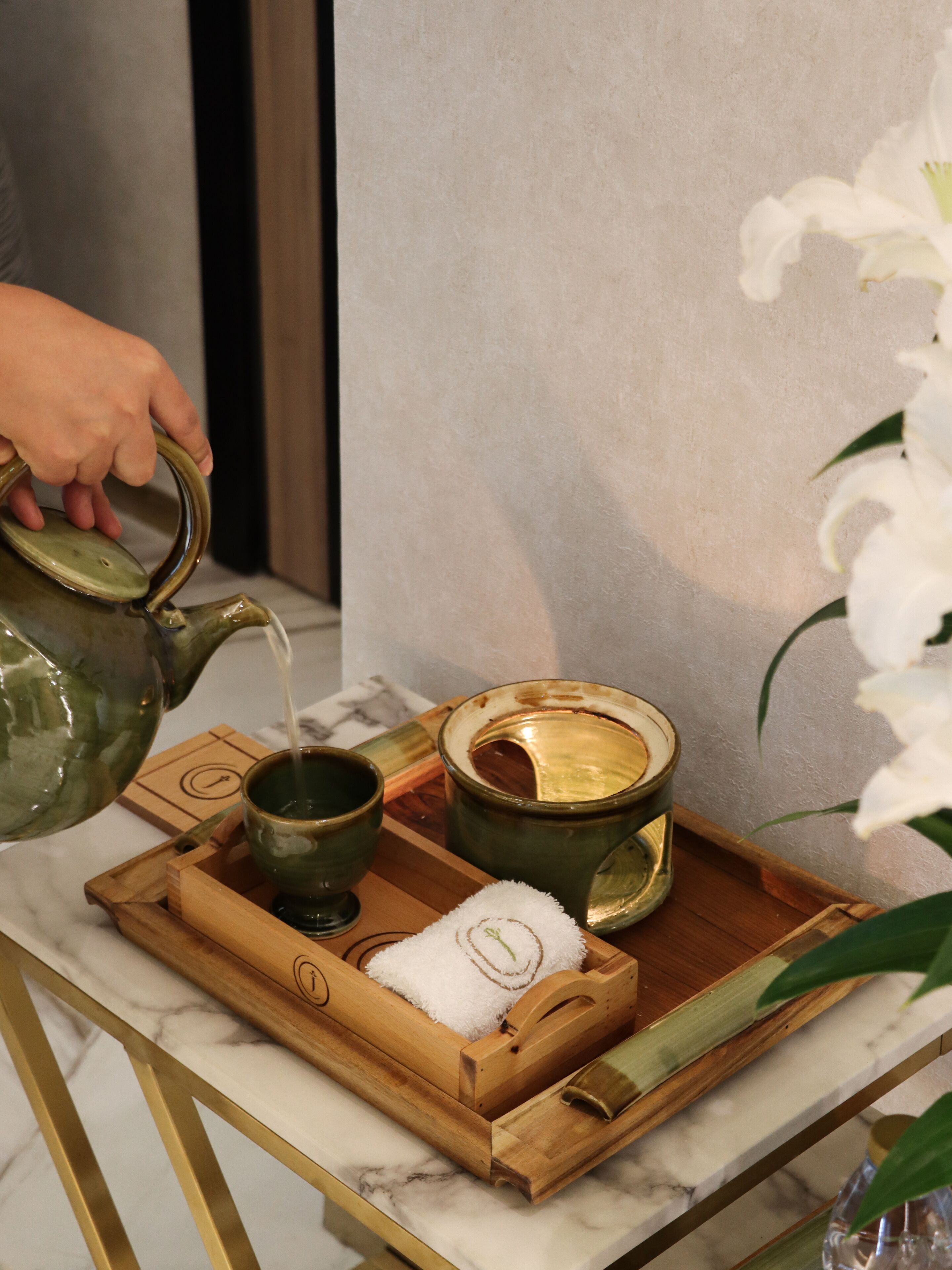 A tray with a teapot, cups, and a towel on a marble countertop.