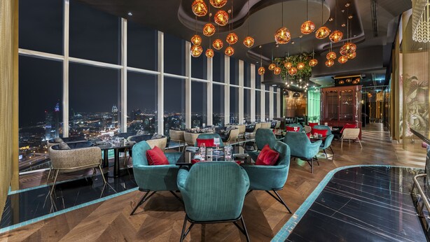 Un restaurant moderne avec de hauts plafonds, des luminaires sphériques suspendus et une vue sur la ville.