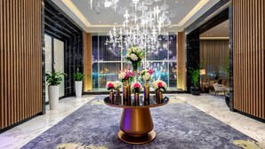 Eine Lobby mit einer zentral platzierten floralen Dekoration auf einem runden Tisch, umgeben von Sitzgelegenheiten und einem großen Fenster mit Blick auf die Stadt.