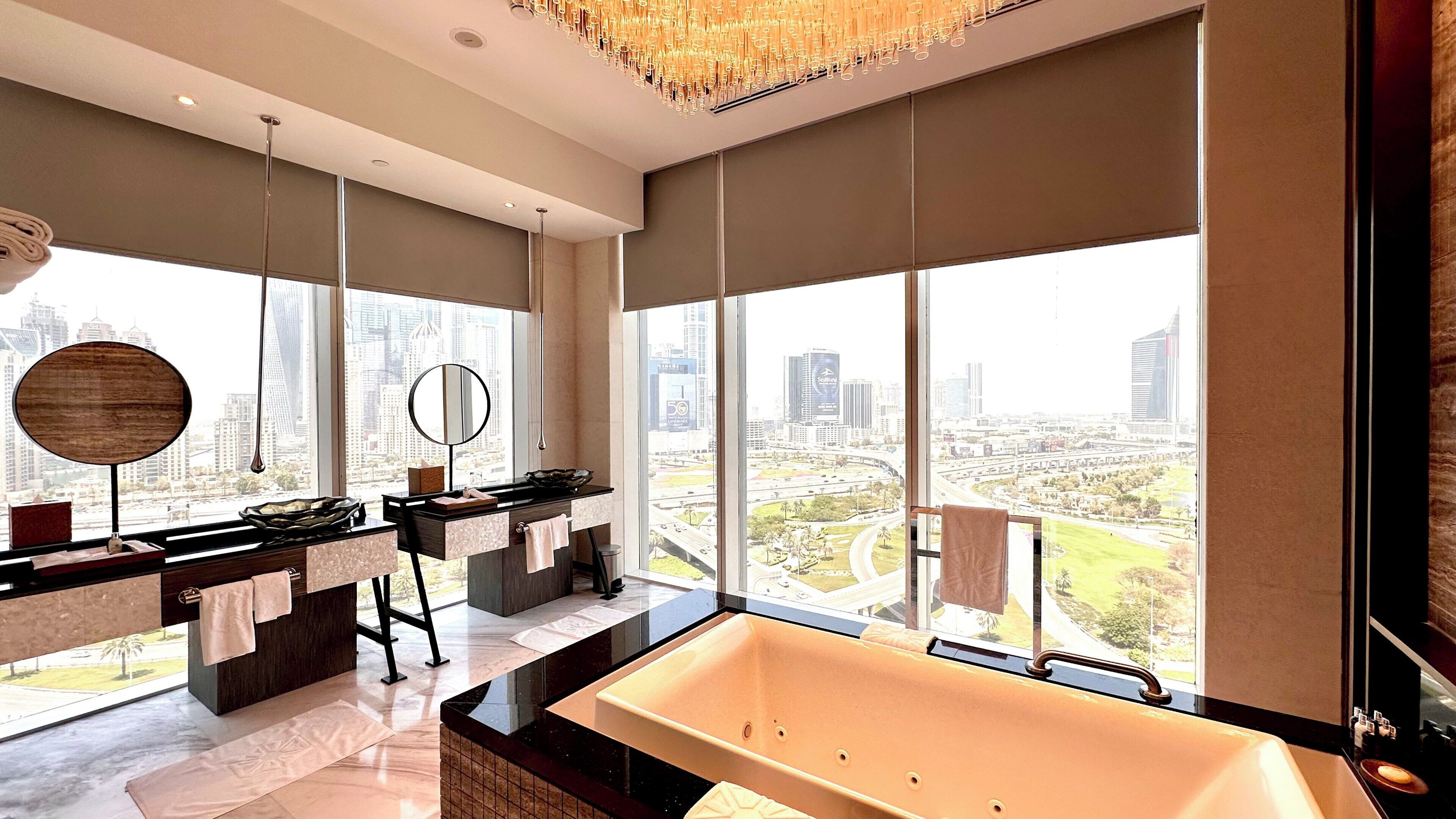 A modern bathroom with a large bathtub, dual sinks, and a city view.