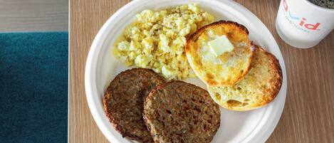 A plate with scrambled eggs, toast with butter, and two patties, accompanied by a coffee cup and a red apple on a wooden table.