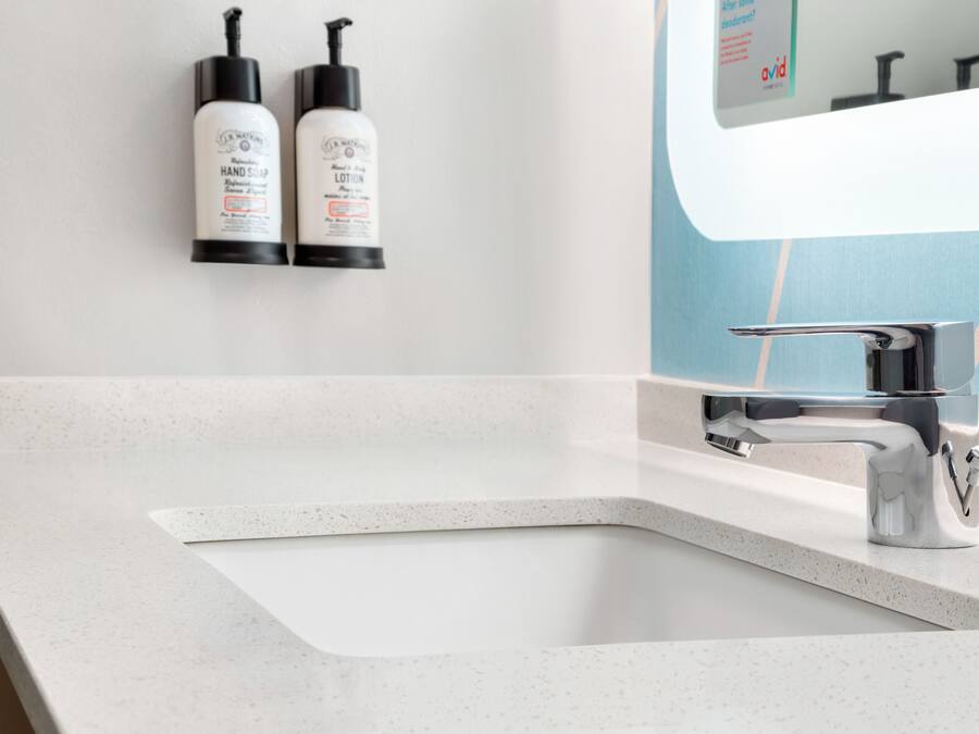 Een badkamer met een witte wastafel, een moderne kraan en twee handzeepflesjes aan de muur bevestigd.