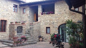 A stone building with a courtyard, steps leading to a door, and potted plants. - Private Room in small medieval borgo (Colle di Val d'Elsa)