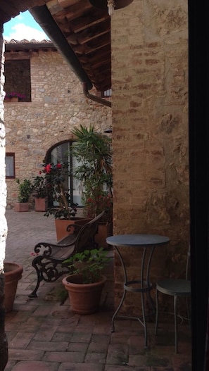 An outdoor patio area with stone walls, potted plants, a bench, and a table. - Private Room in small medieval borgo (Colle di Val d'Elsa)