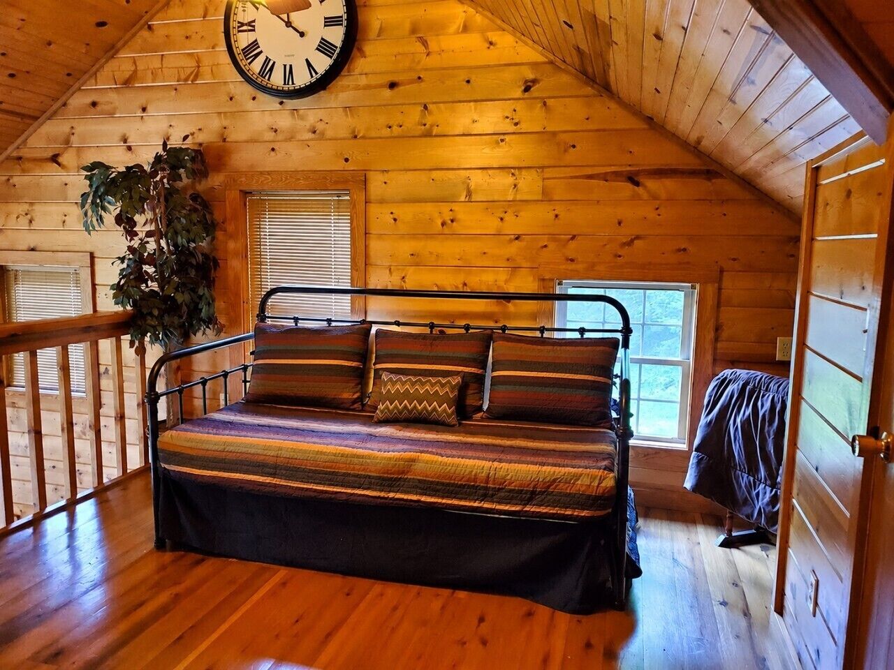 A cozy wooden cabin bedroom with a bed, a large wall clock, and a window.